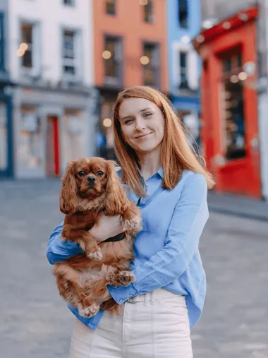 Katya holding a small brown dog on a colorful Edinburgh street