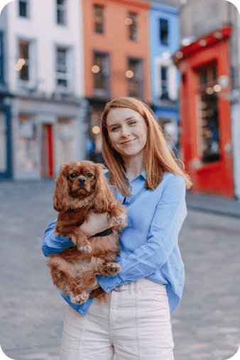 Katya holding a small brown dog on a colorful Edinburgh street